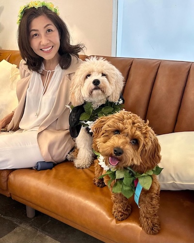 Happy pet owner sitting with two fluffy dogs wearing floral garlands during a NEAT Special appointment in Sherman Oaks